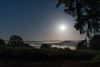 Nebel liegt in einem Tal unter einem sternenklaren Nachthimmel mit hellem Mond, umgeben von Bäumen und Hügeln.