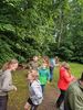 Gruppe von Kindern und Jugendlichen in Outdoor-Kleidung steht auf einer Wiese vor einem Wald mit dichtem Laub.